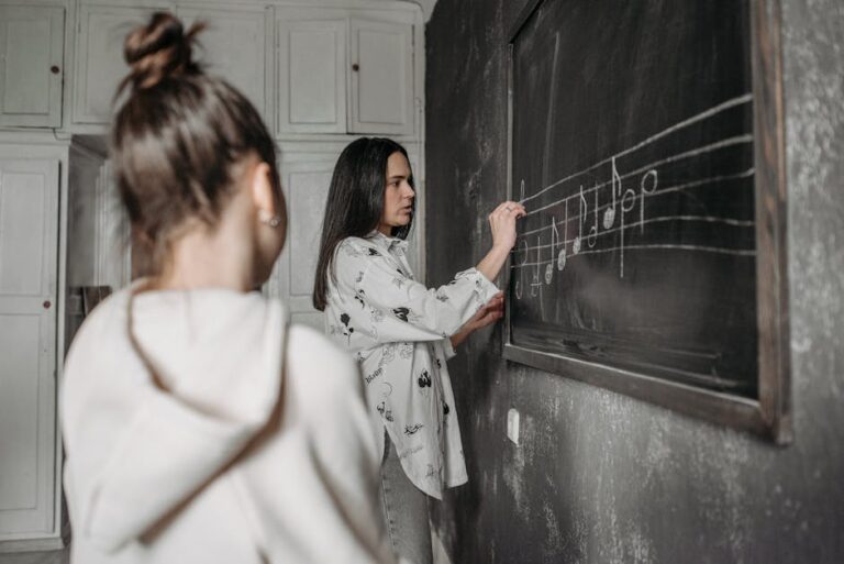 A student observes a teacher writing music notes on a classroom blackboard.